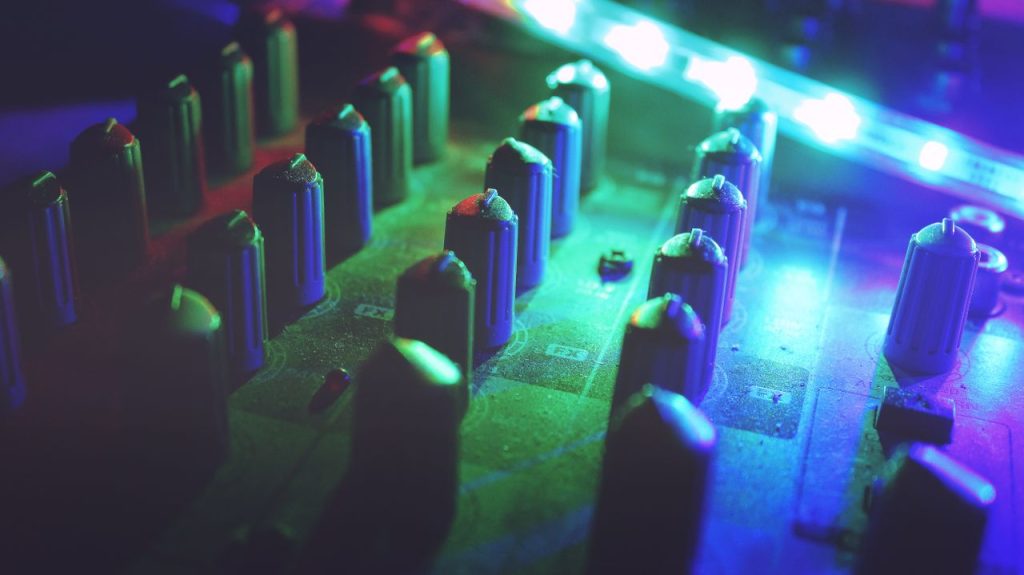 Close-up of a colorful illuminated sound mixer in a dim studio for audio production.